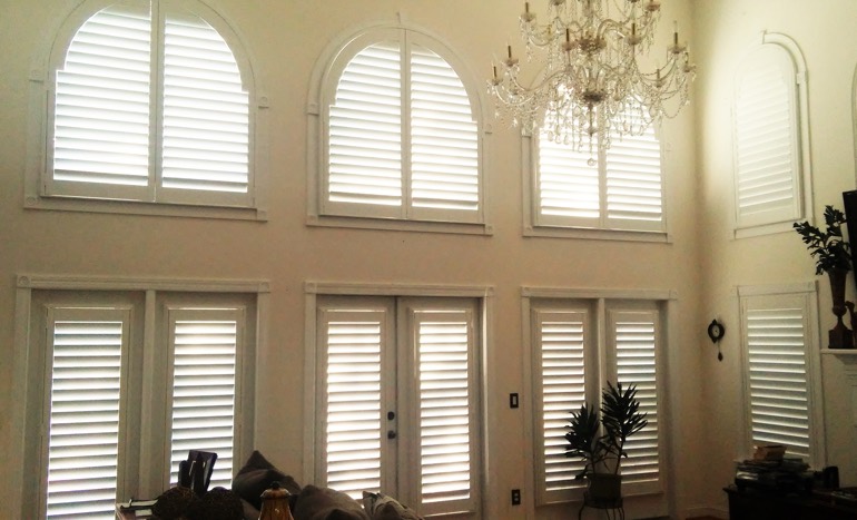 Family room in two-story Orlando house with plantation shutters on arch windows.