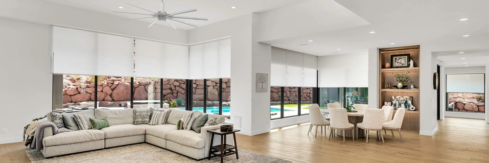 An open concept living area with white window shades on windows looking out on a blue pool