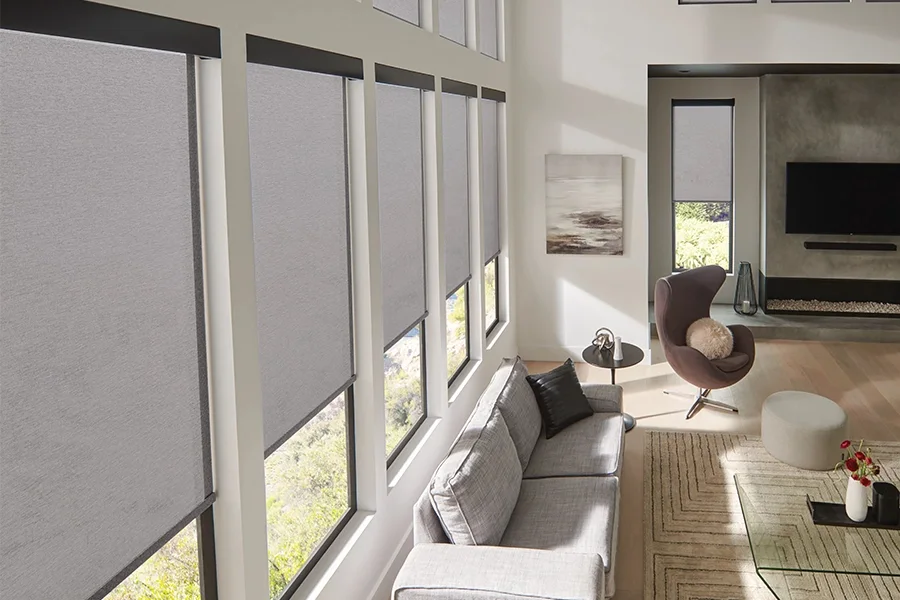 Keep your interior comfortable with heat-blocking solar shades. Grey solar shades on a row of five windows in a living room