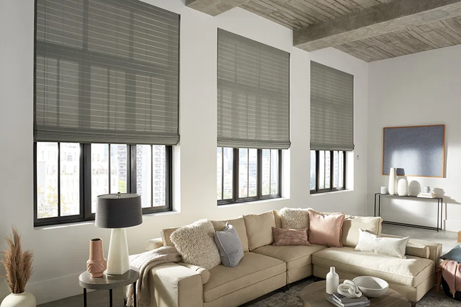 Natural woven shades come in many colors that complement contemporary home decor. Gray woven shades pulled halfway down three windows in a modern living room decorated with neutral colors